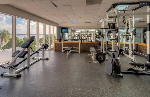 A gym with weightlifting equipment, benches, and a TV screen.
