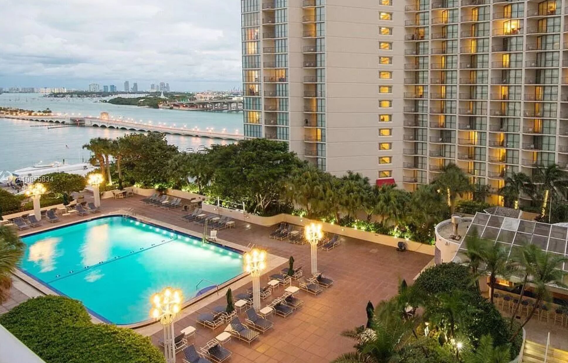 Un espace piscine d’hôtel offrant une vue sur la mer et, en arrière-plan, un immeuble de grande hauteur.