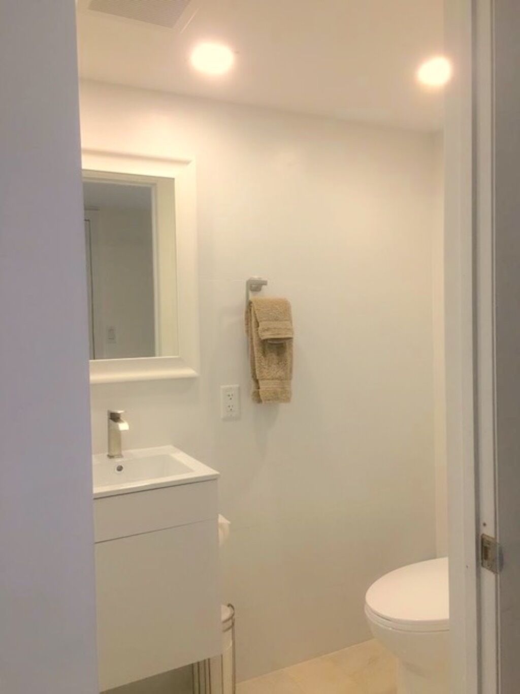 A small, modern bathroom with a white sink, mirror, and toilet.