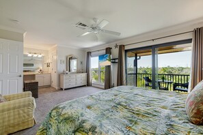 A bedroom with a large bed, a dresser, a vanity, and a balcony with a view.