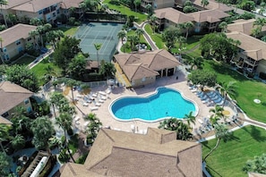 A residential area with a swimming pool surrounded by lounge chairs and palm trees.