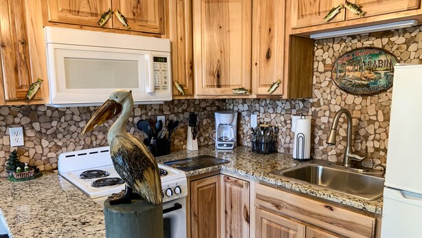 A kitchen with wooden cabinets, a white microwave, a stove, a granite countertop, and a sink.