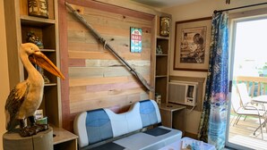 A cozy room with a wooden wall, a blue and white sofa, a pelican statue, a small table, and a suitcase.