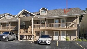 A motel with two-story buildings, a covered parking area, and a white car parked in front.