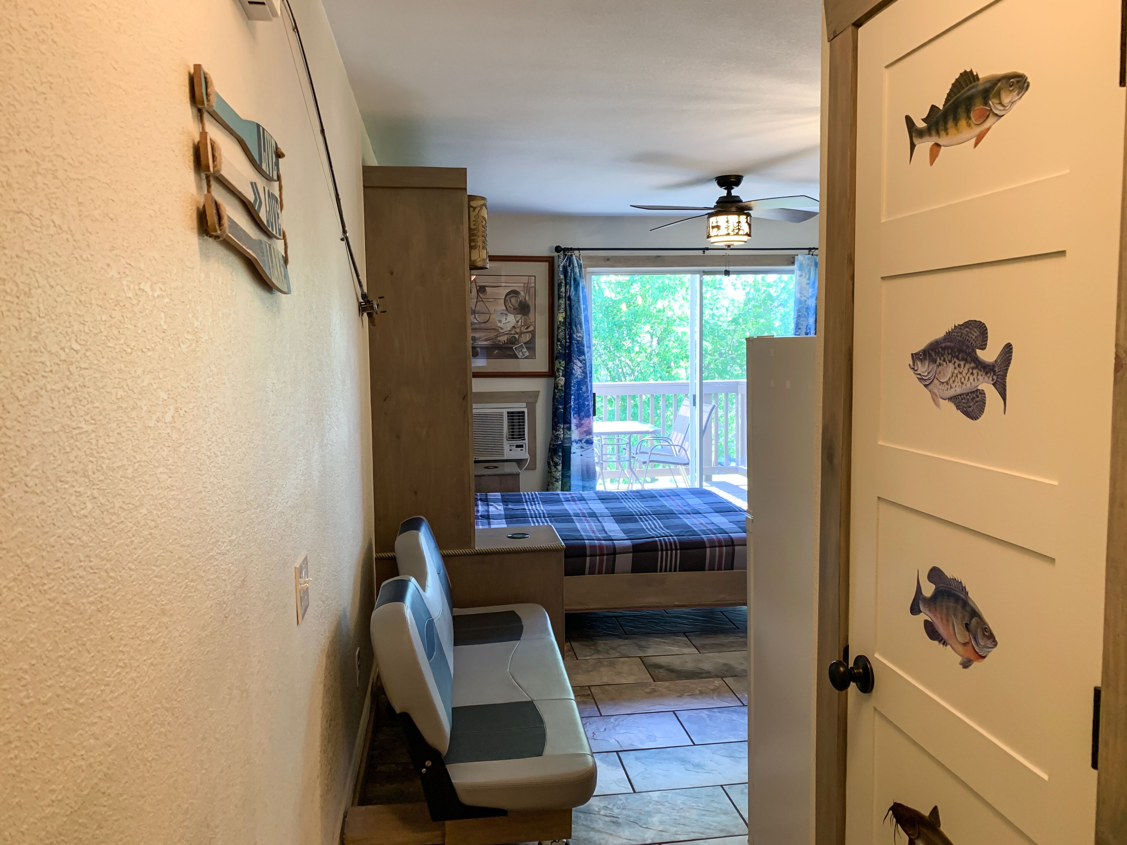 Une pièce comprenant un lit, un banc, un ventilateur de plafond et une porte décorée d’autocollants représentant des poissons.