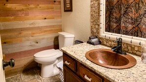 A bathroom with a wooden wall, a white toilet, a copper sink, and a stone-patterned shower curtain.