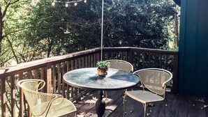 A wooden deck with a round table and four wicker chairs, surrounded by trees and string lights.