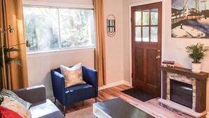 A living room with a blue armchair, a sofa, a fireplace, and a window with curtains.