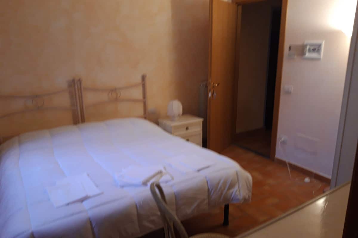 A bedroom with a bed, bedside table, chair, and a door leading to another room.