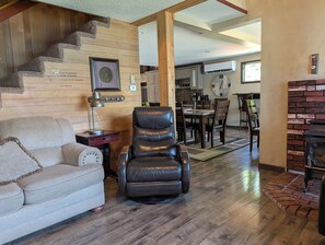 A living room with a sofa, a recliner, a lamp, a fireplace, and a staircase leading to another room.