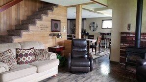 A living room with a staircase, a fireplace, a dining area, and a kitchen in the background.