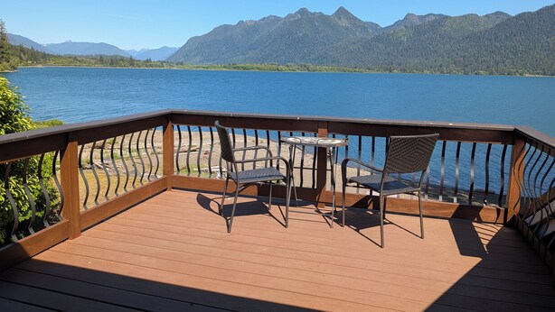 A wooden deck with a table and chairs overlooking a lake and mountains.