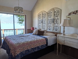 A bedroom with a large bed, a view of a lake, a chandelier, and a decorative wall panel.