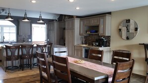A modern kitchen with a central island, bar stools, and a dining table with chairs.