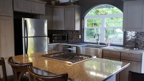 A modern kitchen with granite countertops, stainless steel appliances, and a large window overlooking a garden.