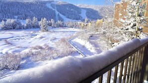 Schneelandschaft mit freiem Blick auf einen Berg, eine Skipiste und ein Gebäude mit Balkon.