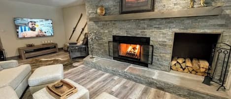 A living room with a stone fireplace, a television, and a fireplace mantel with decorative items.