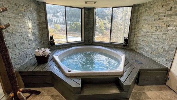 Ein Whirlpool in einer Ecke mit Steinwänden und großen Fenstern.