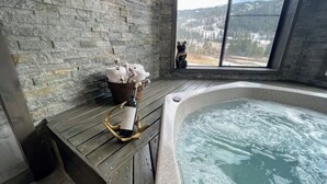 Ein Zimmer mit Steinwänden, einer hölzernen Bank, einer Flasche und einer Bärenfigur an einem Fenster mit Blick auf eine verschneite Landschaft.