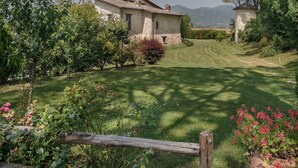 Ein Steinhhaus mit gepflegtem Rasen und Garten, umgeben von Bäumen und Bergen im Hintergrund.