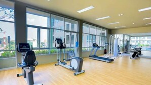 A gym with cardio machines, weight training equipment, and large windows offering a city view. - Lumpini Ville Pattaya Pool Gym (Pattaya)