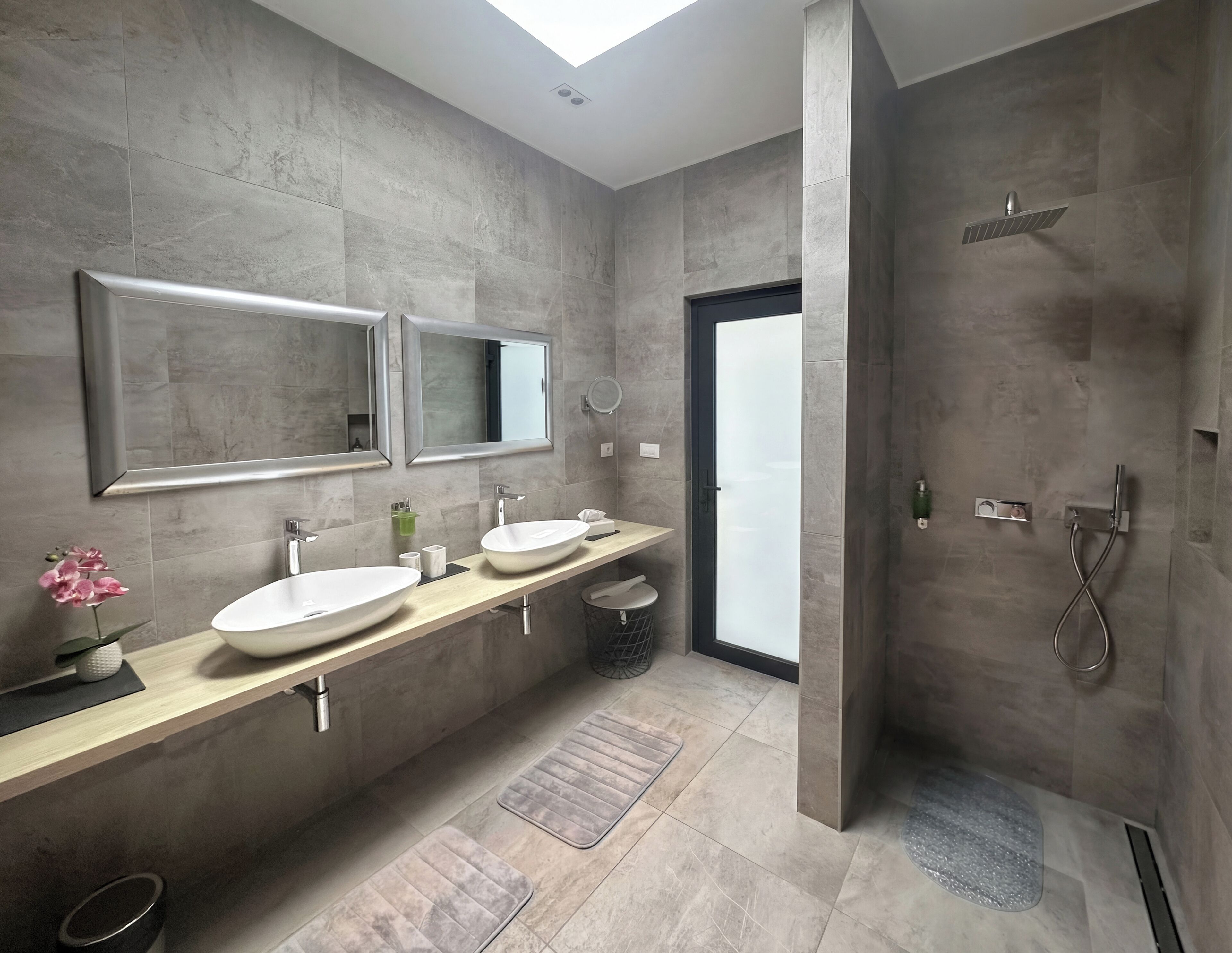 Een moderne badkamer met twee wastafels, een grote spiegel en een ruime douche.