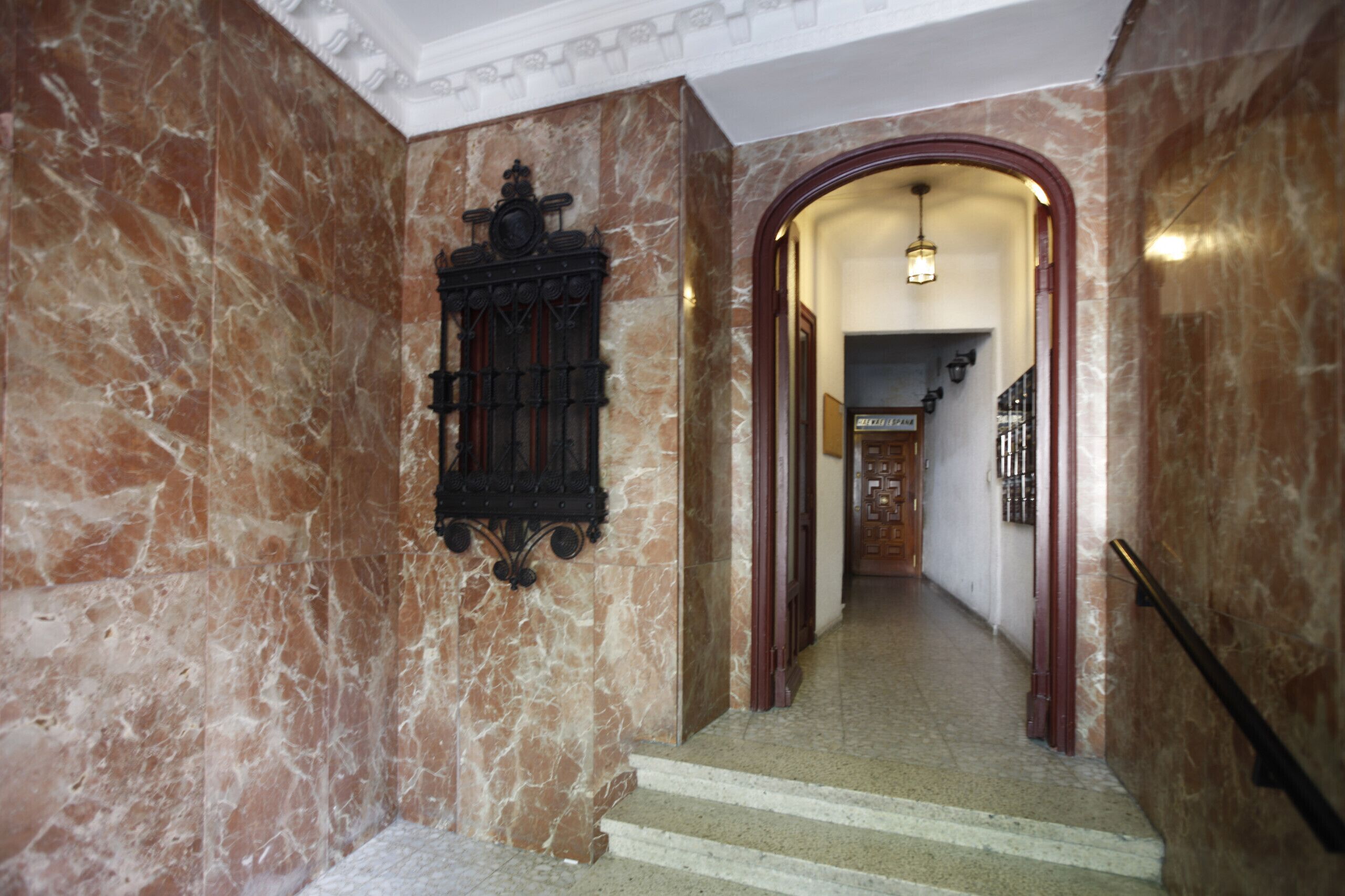 A marble staircase leading to a hallway with a wooden door and a hanging light fixture.