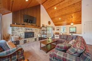 A cozy living room with a stone fireplace, plaid furniture, and a wooden ceiling.