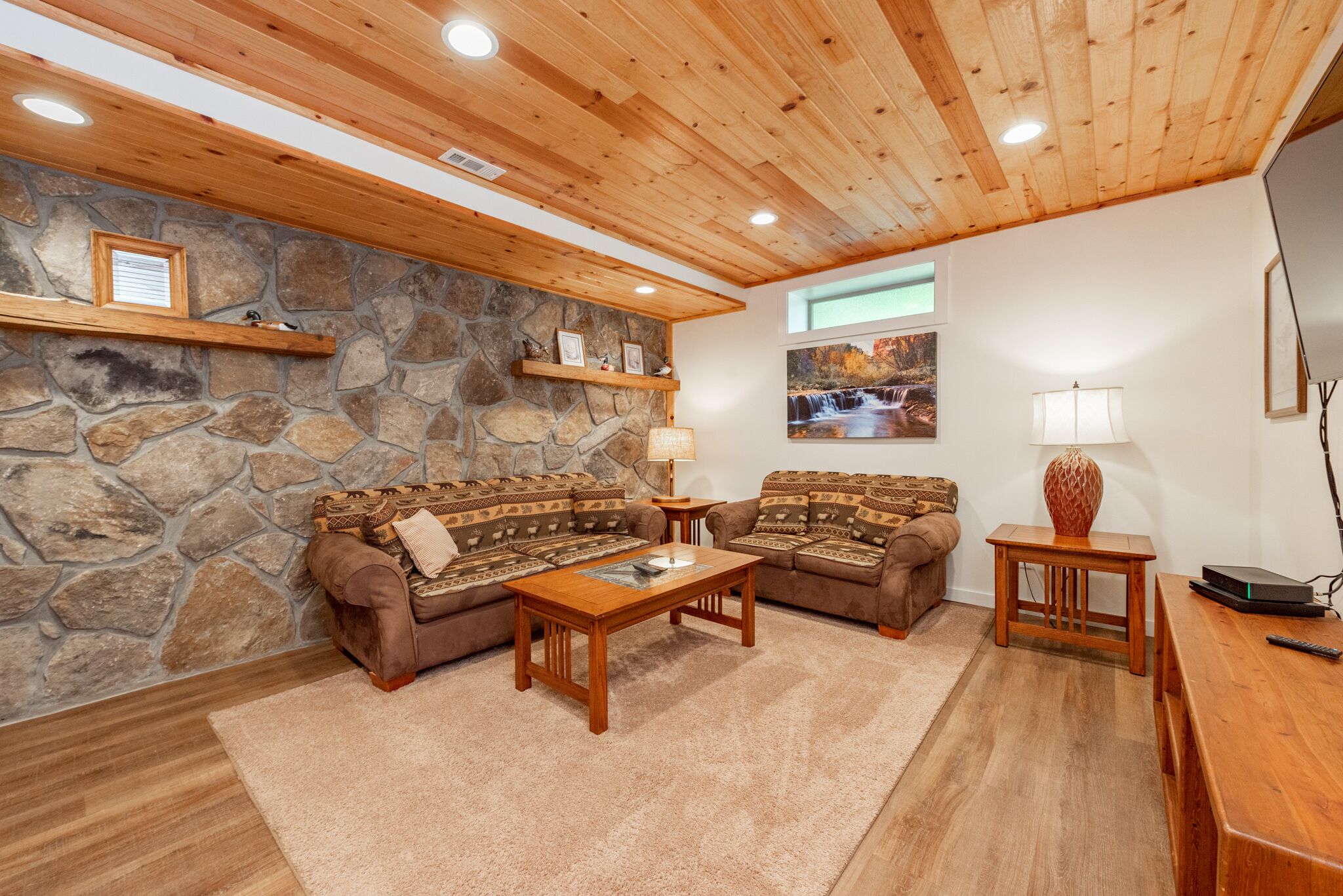 Una sala de estar acogedora con pared de piedra, techo de madera y dos sofás estampados.