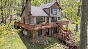 Une cabane à deux étages, avec des fondations en pierre, une terrasse en bois et un escalier menant à l’étage supérieur.