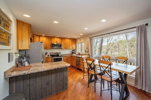 A kitchen with wooden cabinets, a granite countertop, a dining table with chairs, and a view through large windows.