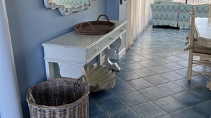 A room with a large mirror, a white console table, wicker baskets, and a view of the beach through large windows. - Panoramic Oceanfront. Beautiful Five Star. The get-away for any season. (Bethany Beach)