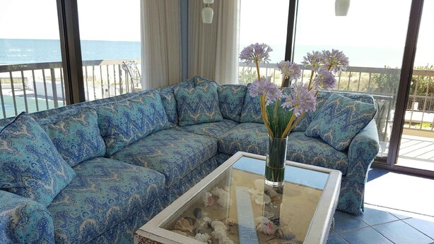 A blue patterned sofa with a glass coffee table and a vase of flowers. - Panoramic Oceanfront. Beautiful Five Star. The get-away for any season. (Bethany Beach)