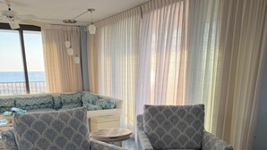 A living room with patterned armchairs, a sofa, a small table, and a view of the sea through large windows. - Panoramic Oceanfront. Beautiful Five Star. The get-away for any season. (Bethany Beach)
