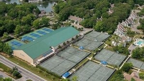 An aerial view of a residential area with multiple tennis courts, a large green-roofed building, and surrounding houses. - Panoramic Oceanfront. Beautiful Five Star. The get-away for any season. (Bethany Beach)