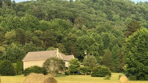 Paisatge rural amb una casa, farquetes de fenc i un bosc dens.