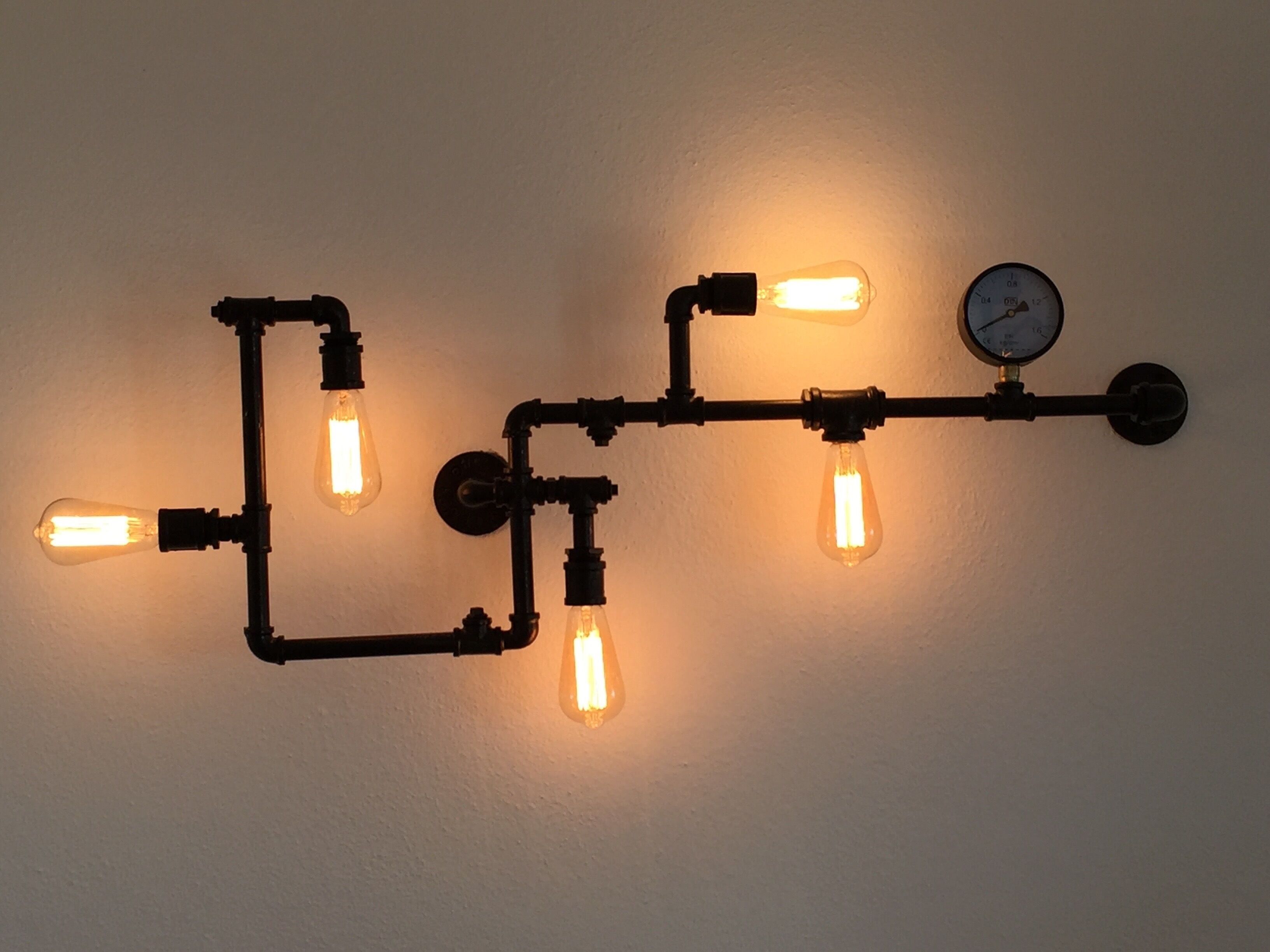 A wall-mounted light fixture with exposed pipes and bulbs.