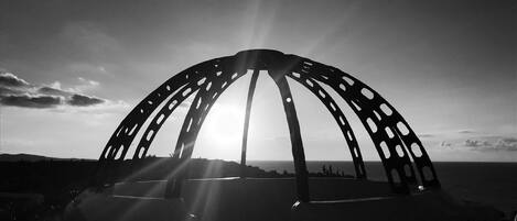 A black and white photo of a large, arched metal structure with multiple openings, set against a backdrop of a clear sky and distant landscape.