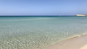 A clear beach with shallow water and a distant rocky outcrop. - Luxury Villa, Breathtaking 180° Sea & Sunset views, Private Pool. Fully AC (San Jaime Mediterráneo, Son Bou, Menorca)