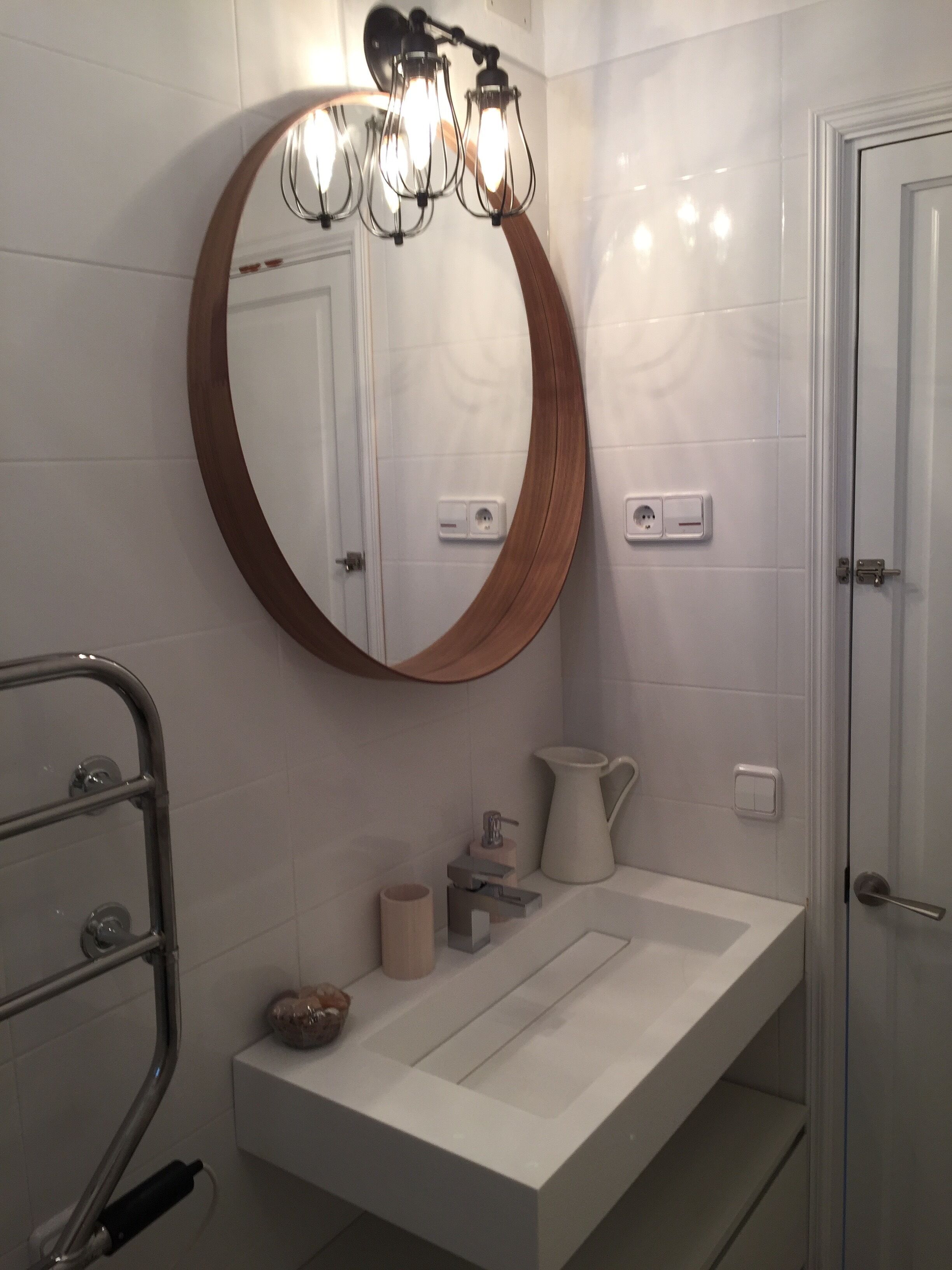 Ein Badezimmer mit rundem Spiegel, weißem Waschbecken, Handtuchhalter und Duschbereich.