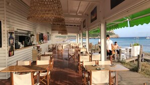 An outdoor dining area with wooden tables and chairs, a bar counter, and a view of the sea. - Luxury Villa, Breathtaking 180° Sea & Sunset views, Private Pool. Fully AC (San Jaime Mediterráneo, Son Bou, Menorca)