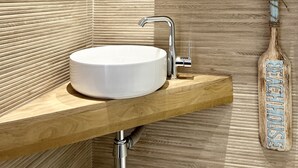 A bathroom with a round white sink, a modern faucet, a wooden vanity, a mirror, and a towel holder with a towel.