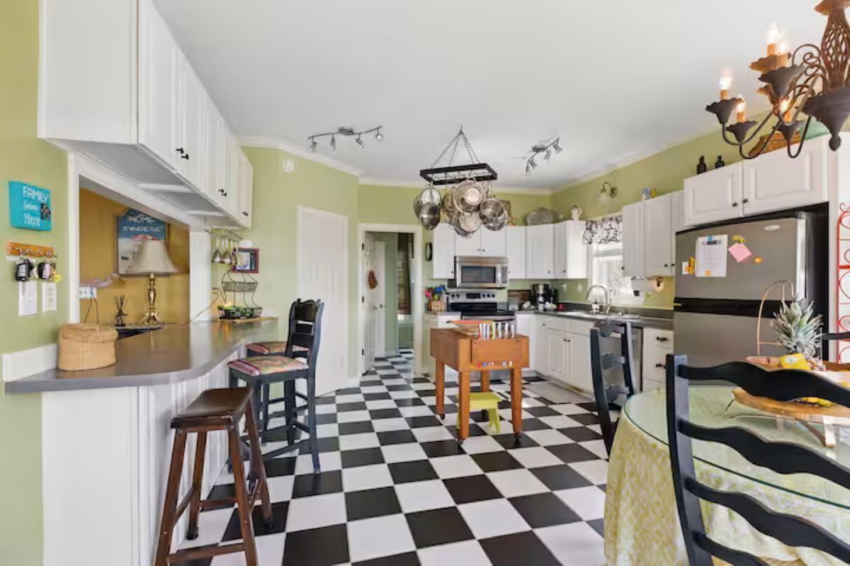 A kitchen with white cabinets, a black and white checkered floor, a chandelier, and a refrigerator.