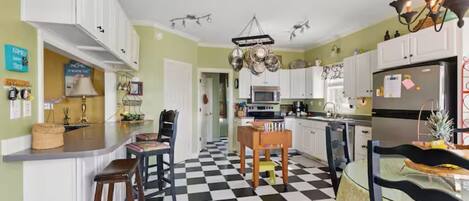 A kitchen with white cabinets, a black and white checkered floor, a chandelier, and a refrigerator.
