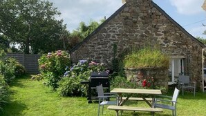 Una casa in pietra con un camino, un barbecue e un tavolo da picnic in un giardino.