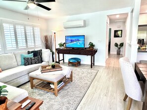 Sala de estar com sofá, mesa de centro, TV e um espaço de refeições com uma cadeira.