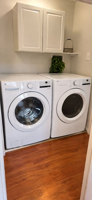 A laundry room with two white front-loading washing machines, wooden flooring, and white cabinets above.