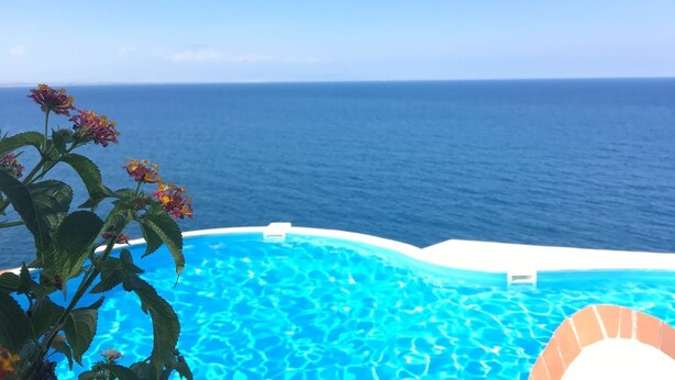 A pool with clear blue water, surrounded by a white deck, and overlooking a vast ocean under a clear sky.