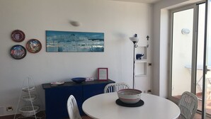 A dining area with a round table, white chairs, a blue cabinet, and a wall-mounted painting.