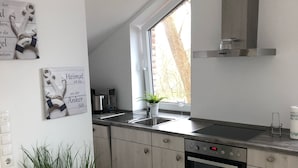 Une cuisine moderne avec des meubles de couleur bois clair, un four encastré et une fenêtre donnant sur la verdure.